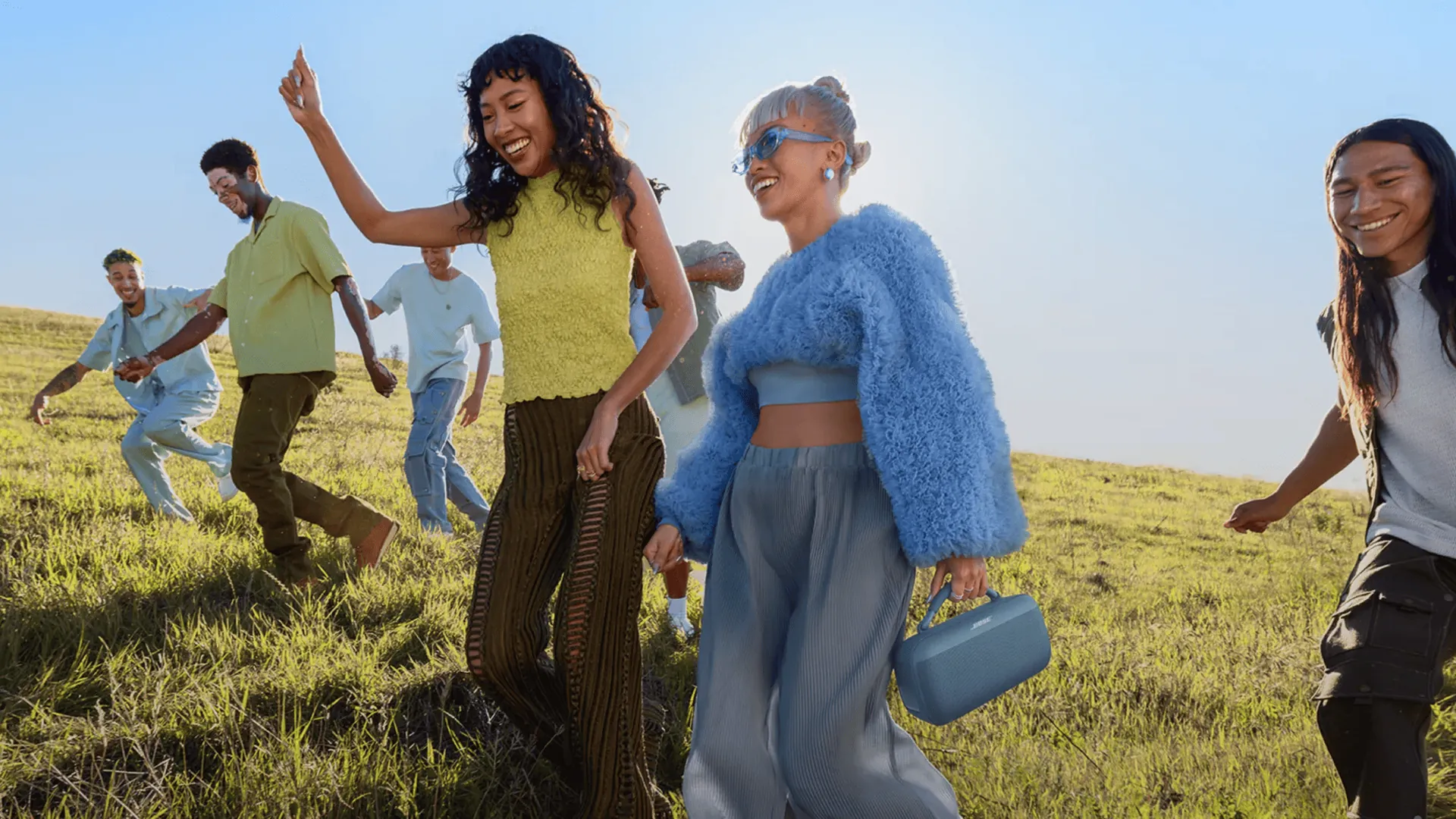 Amigos bailando al aire libre con un SoundLink Max azul atardecer