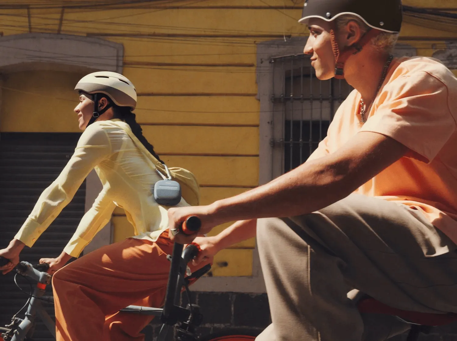 Dos personas en bicicleta con un SoundLink Micro azul atardecer colgado de la mochila