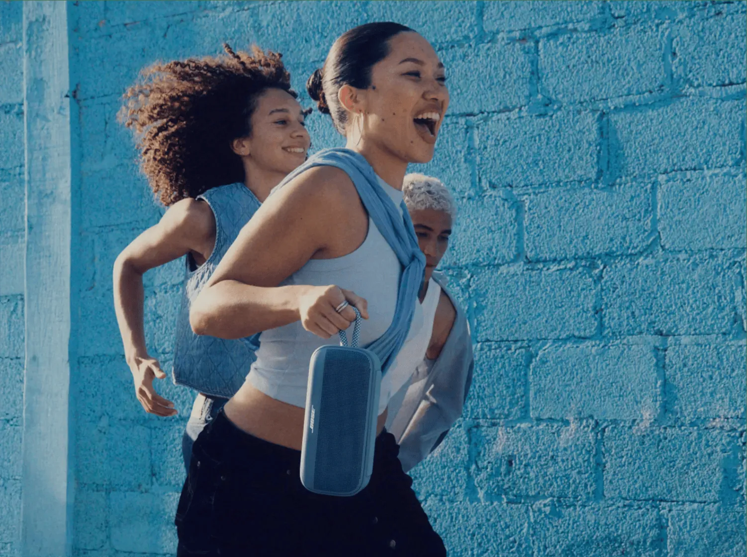 Chicas corriendo con un SoundLink Plus azul atardecer en la mano