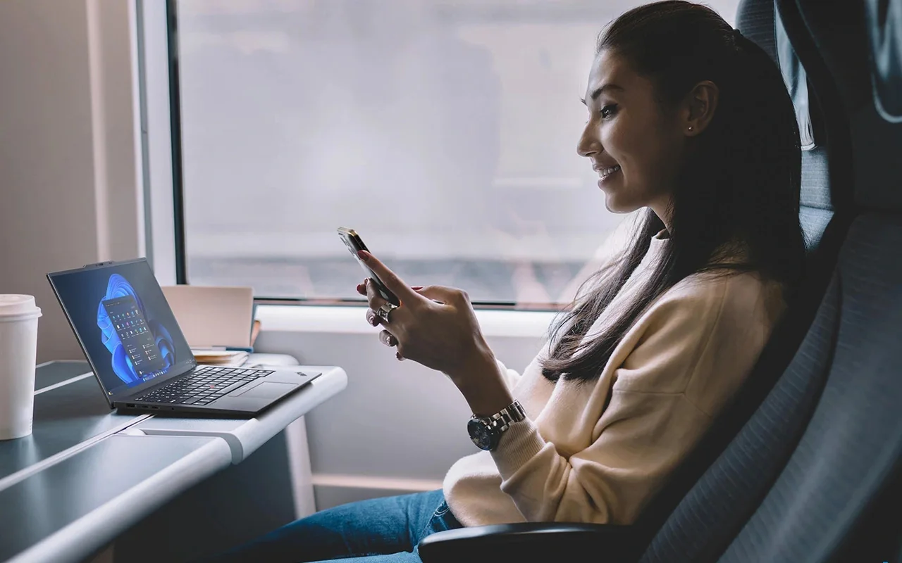 Mujer en un tren con su celular y una ThinkPad X1 Carbon abierta